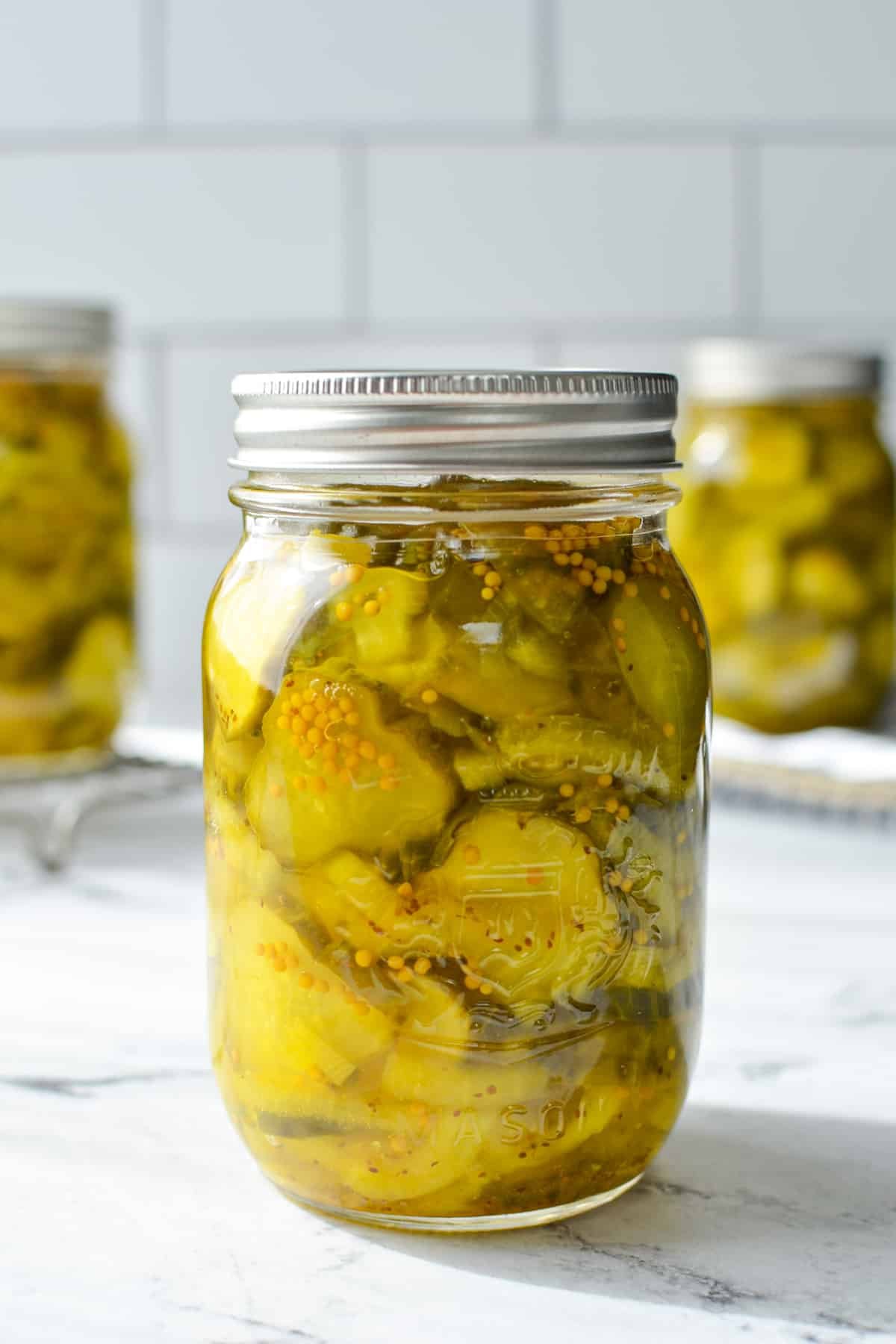 A jar of bread and butter pickles on a white marble background.