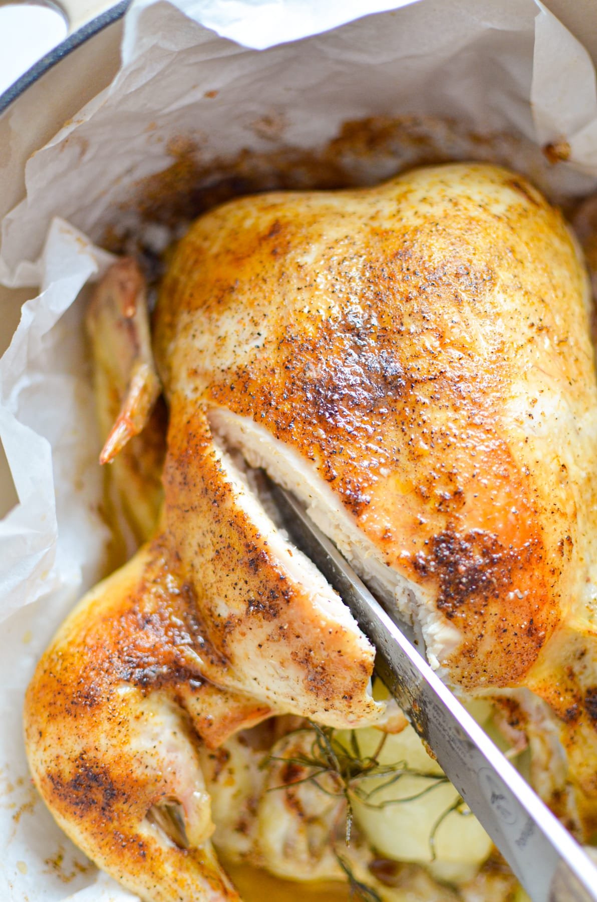 An overhead view of a whole chicken with a knife slicing into it.