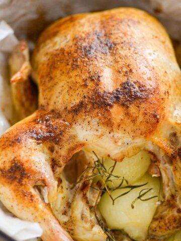 A close up of a whole roast chicken with onions and rosemary.