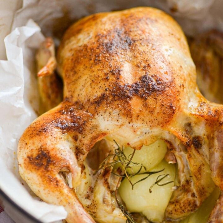 A close up of a whole roast chicken with onions and rosemary.