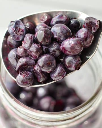 A spoonful of blueberries from a jar.