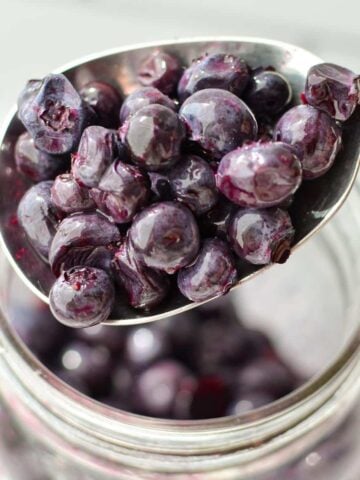 A spoonful of blueberries from a jar.