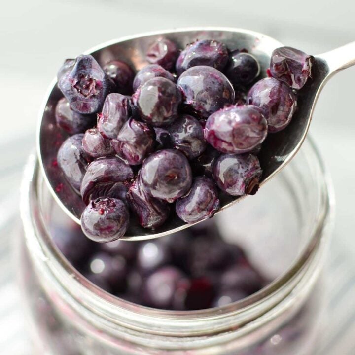 A spoonful of blueberries from a jar.