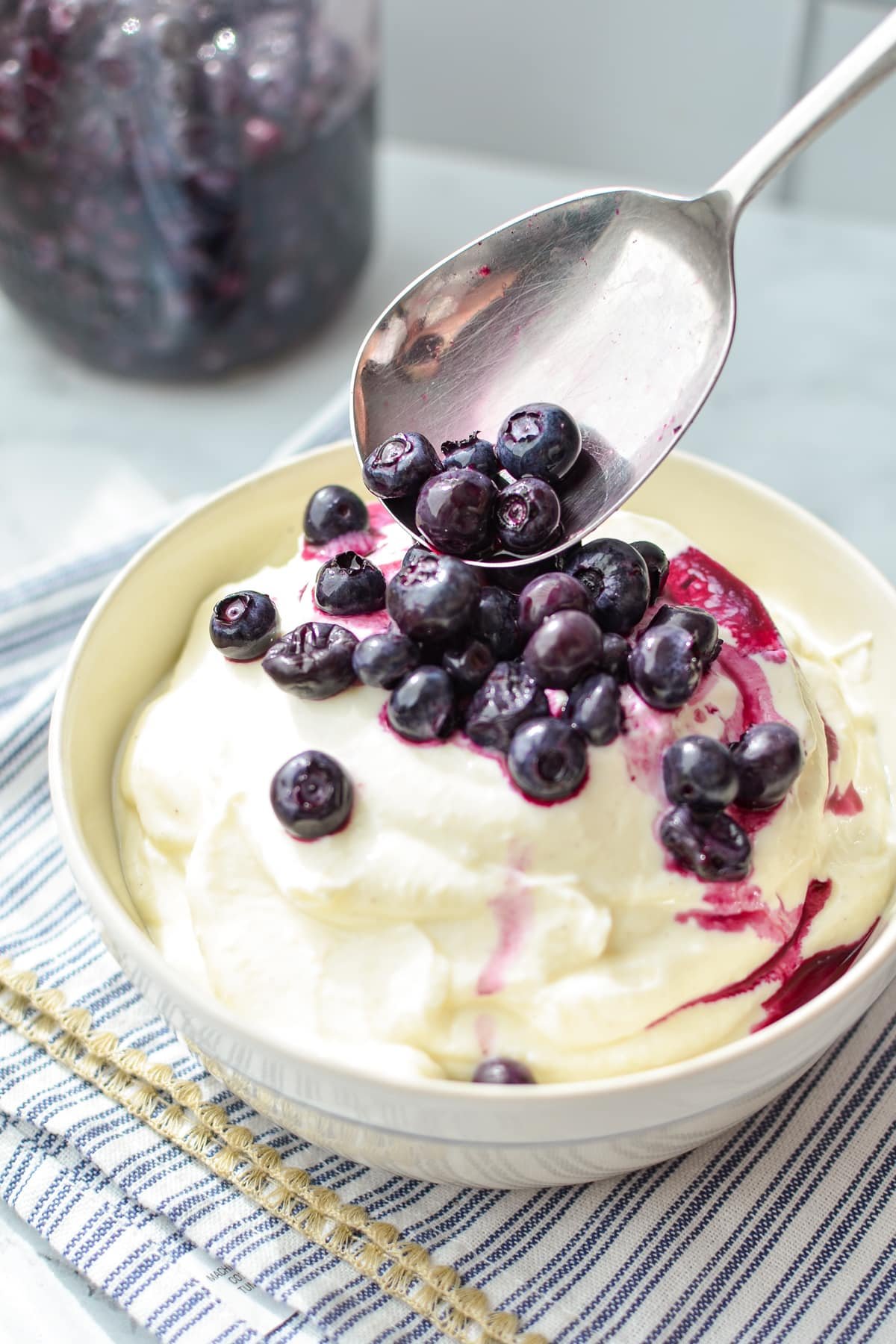 Spooning blueberries onto a bowl of yogurt.