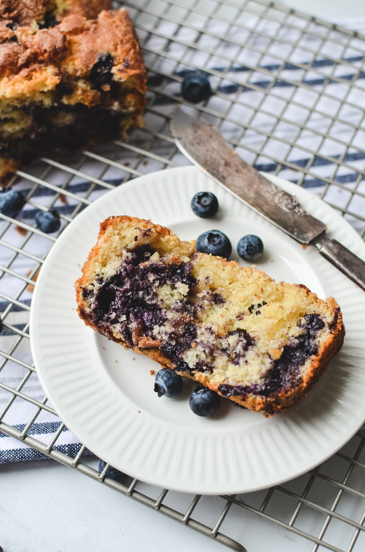 A slice of blueberry bread on a white plate with the loaf in the background.