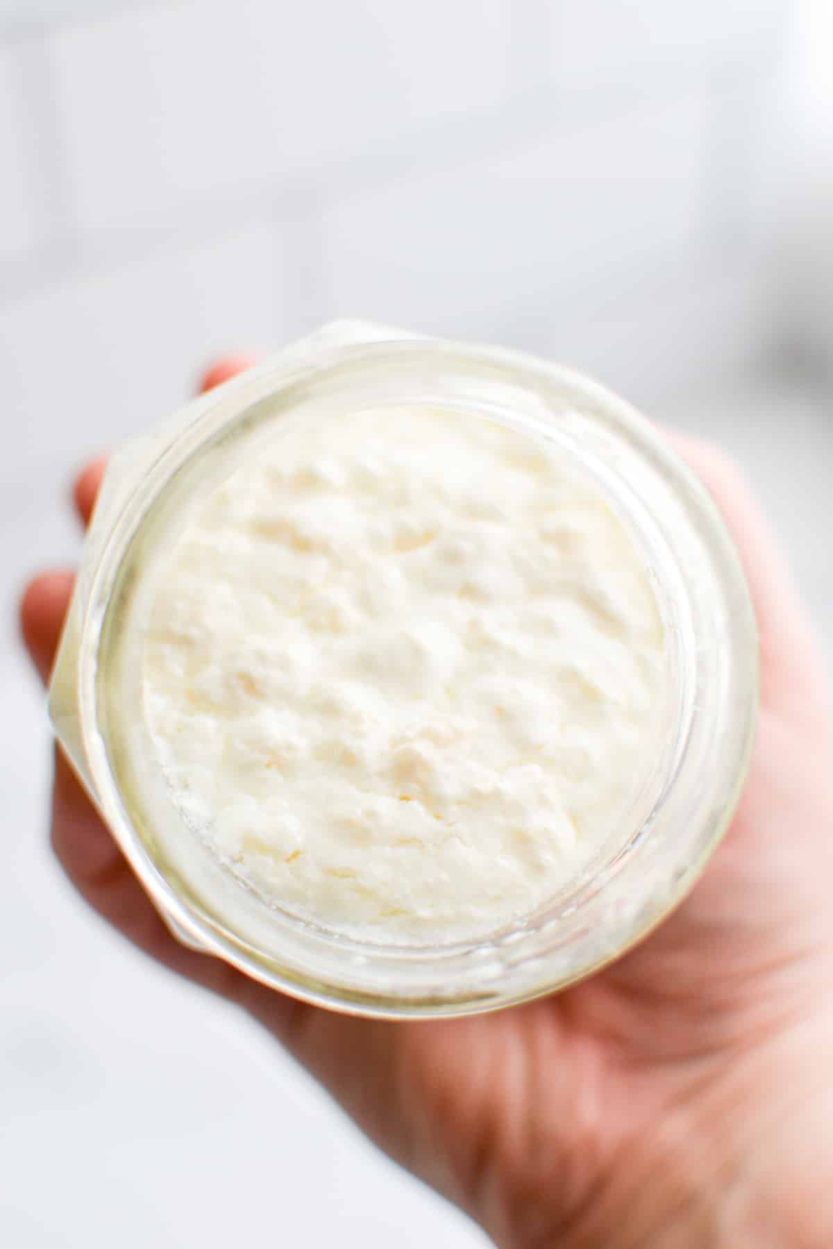 A jar of kefir being held up, with the grains floating to the top.