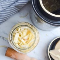 An overhead shot of a jar of sauerkraut with a fermentation crock in the corner.