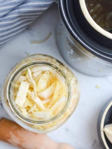 An overhead shot of a jar of sauerkraut with a fermentation crock in the corner.