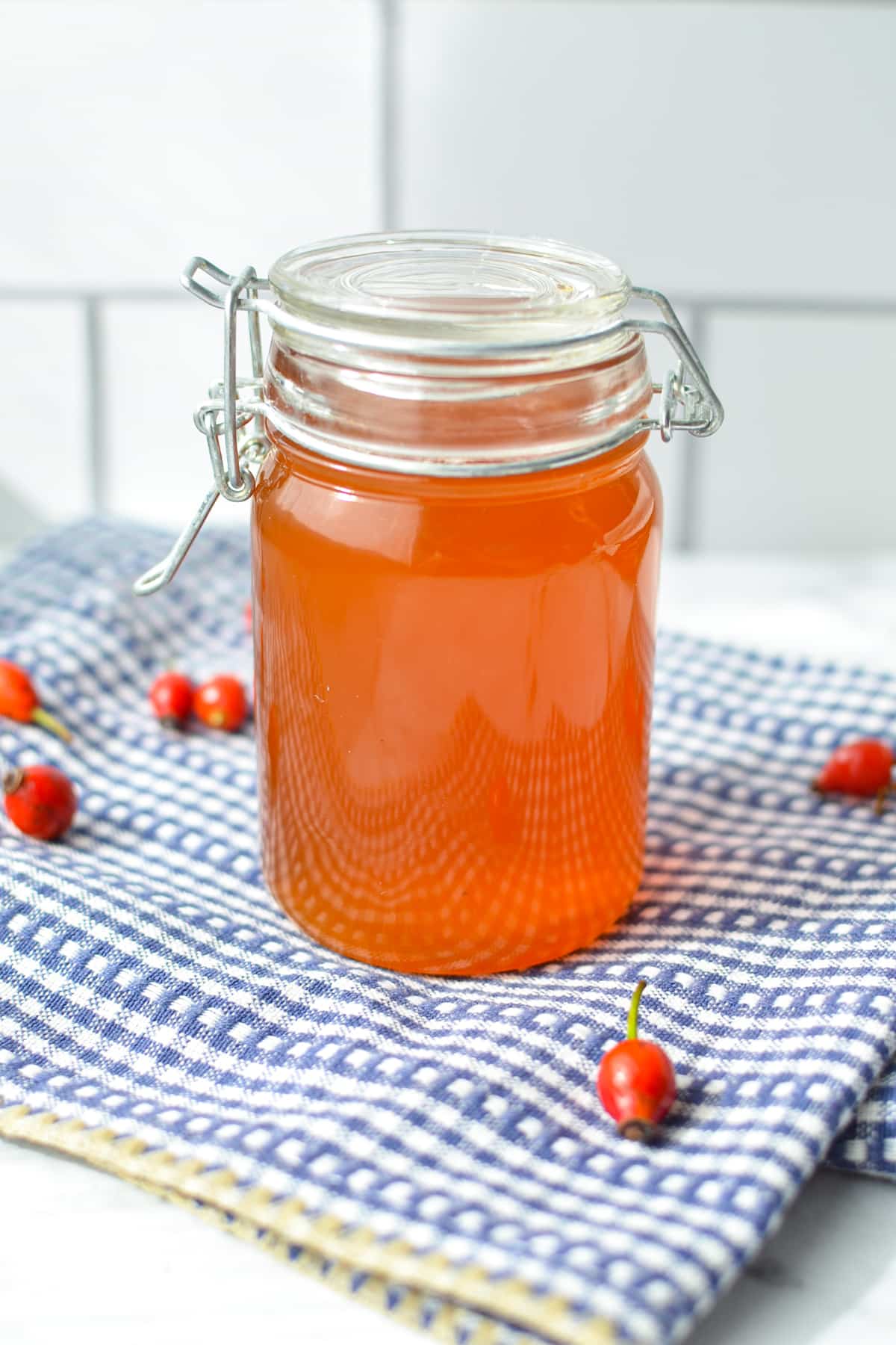 A small jar of rosehip syrup on a blue cloth.