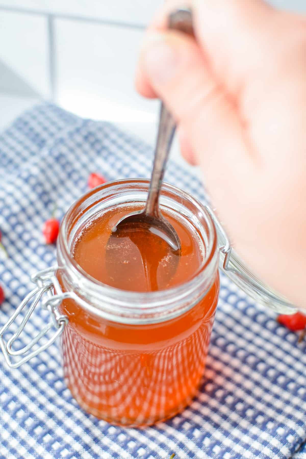 A small jar of rosehip syrup with a spoon dipping into it.