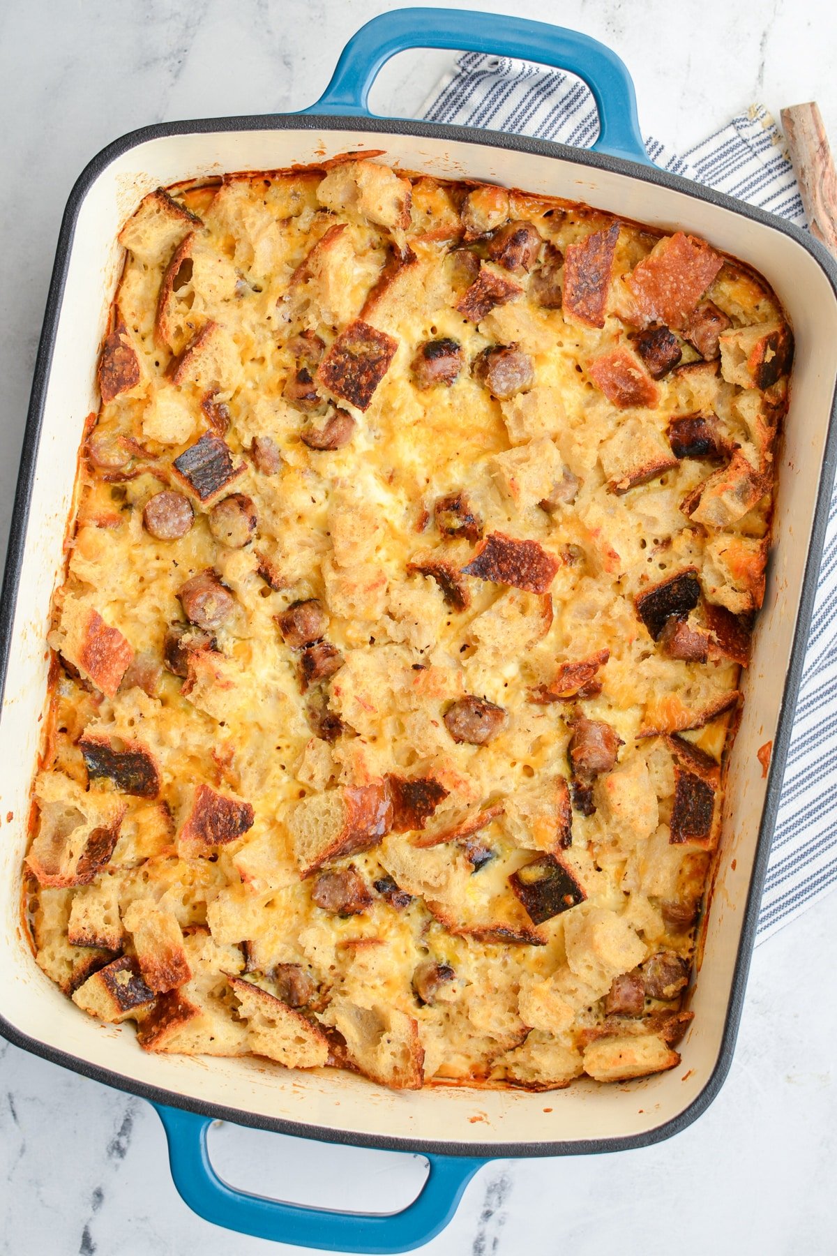 A casserole dish filled with a breakfast casserole with eggs, bread, and sausage.