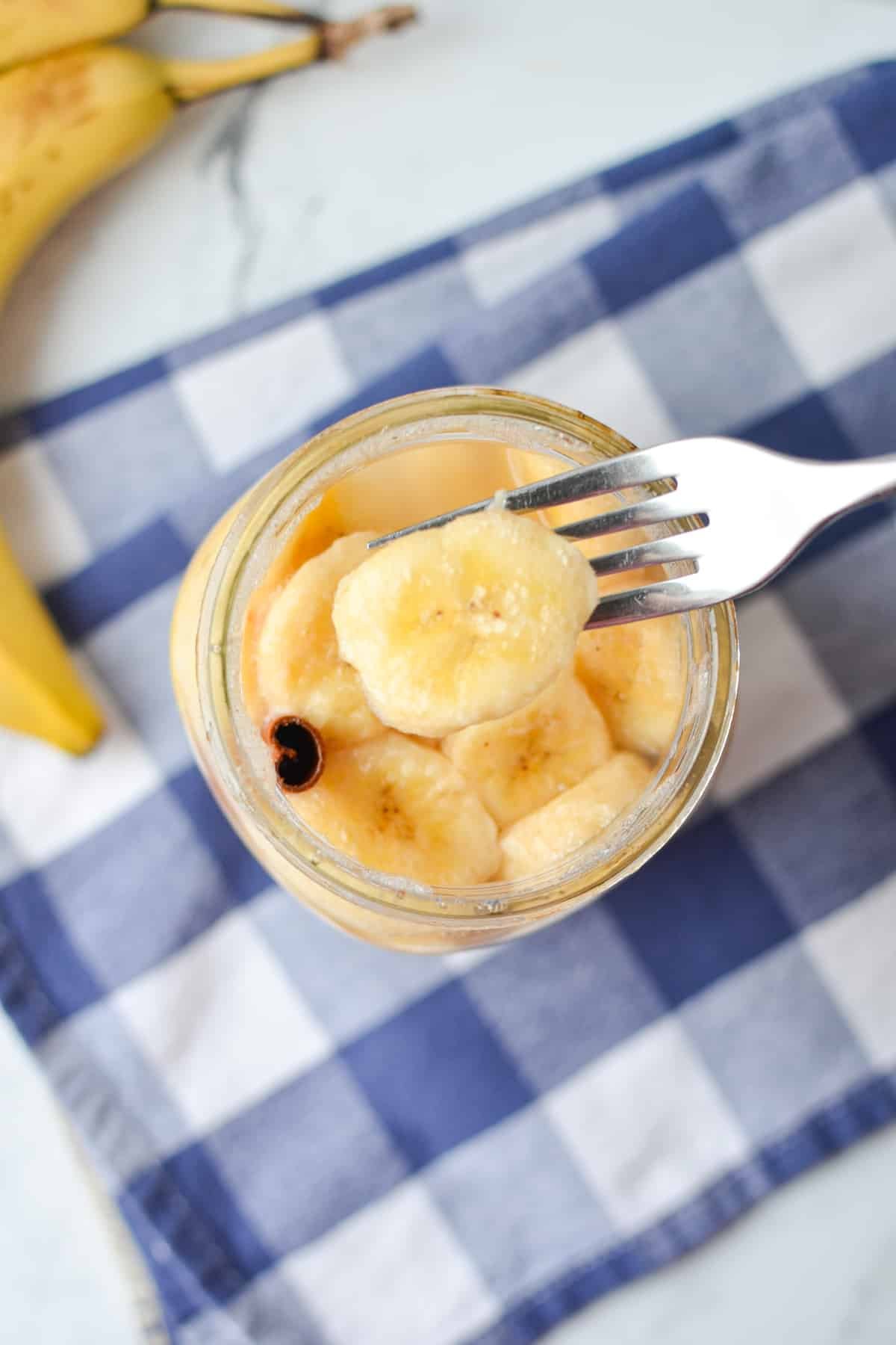 Taking a banana slice from a jar with a fork.