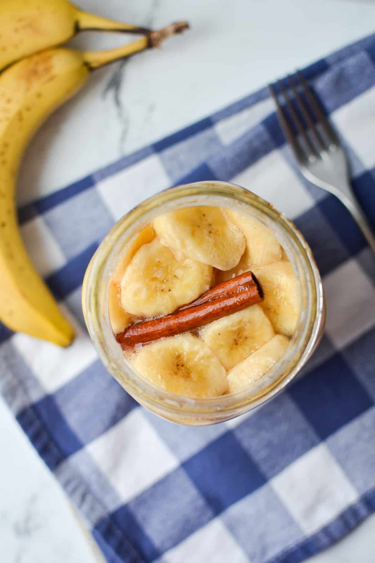 An overhead image of a jar filled with banana slices and a cinnamon stick.