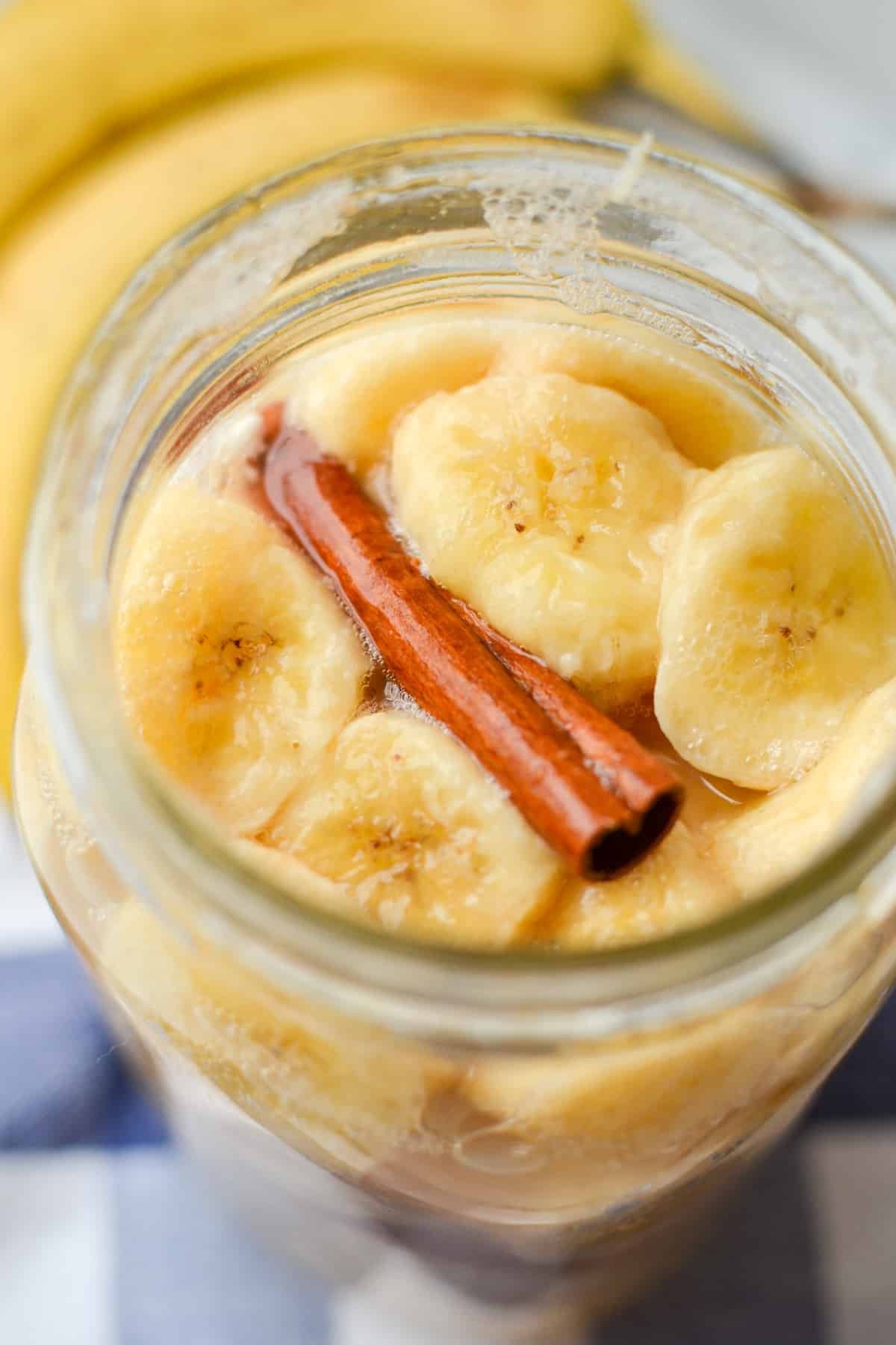 A jar with soft sliced bananas and a cinnamon stick.