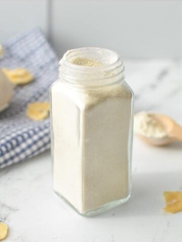 A jar of garlic powder with garlic cloves in the background.