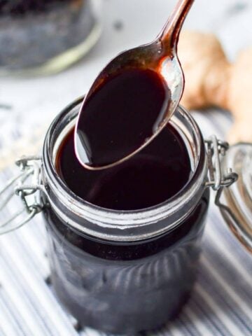 A spoon taking a portion from a jar of elderberry syrup.