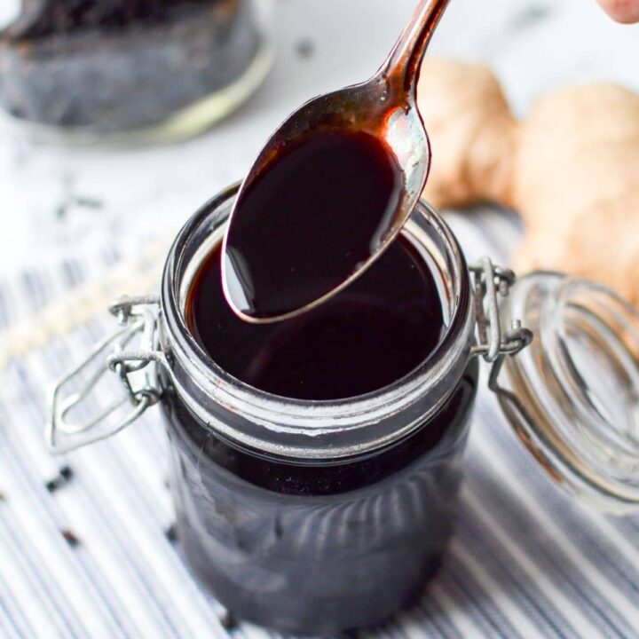A spoon taking a portion from a jar of elderberry syrup.