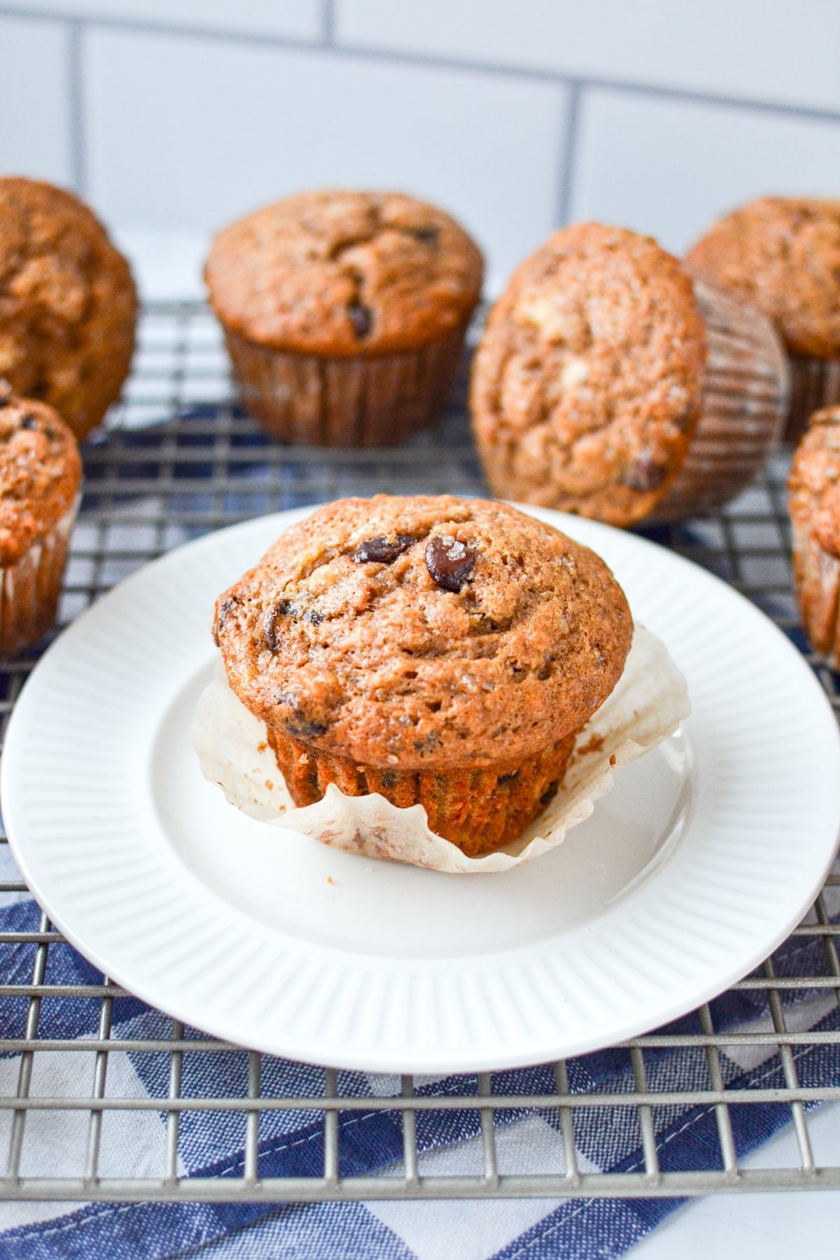 A banana muffin on a plate, surrounded by muffins on a cooling rack.