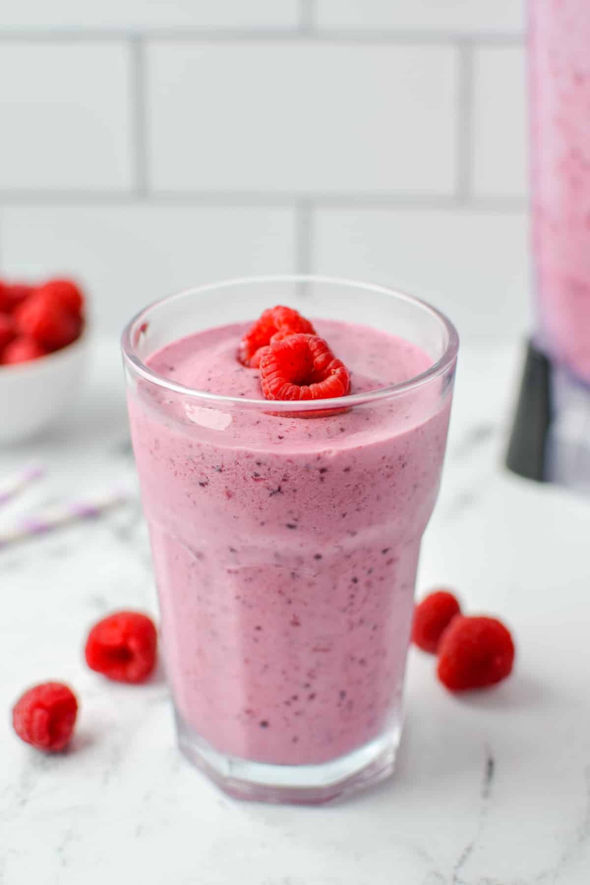 A glass filled with a smoothie and topped with fresh raspberries.