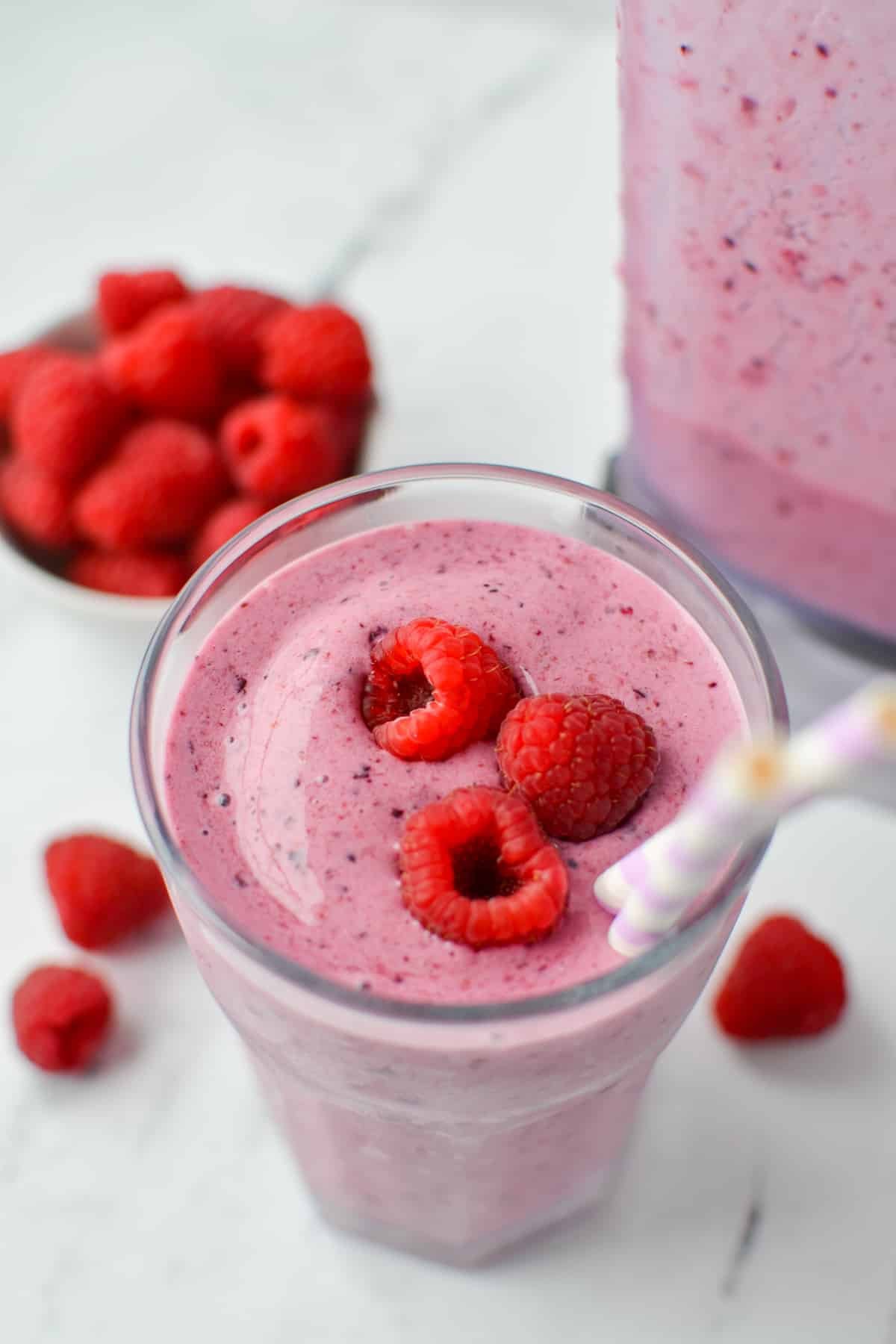 A glass filled with a berry smoothie, topped with fresh raspberries.