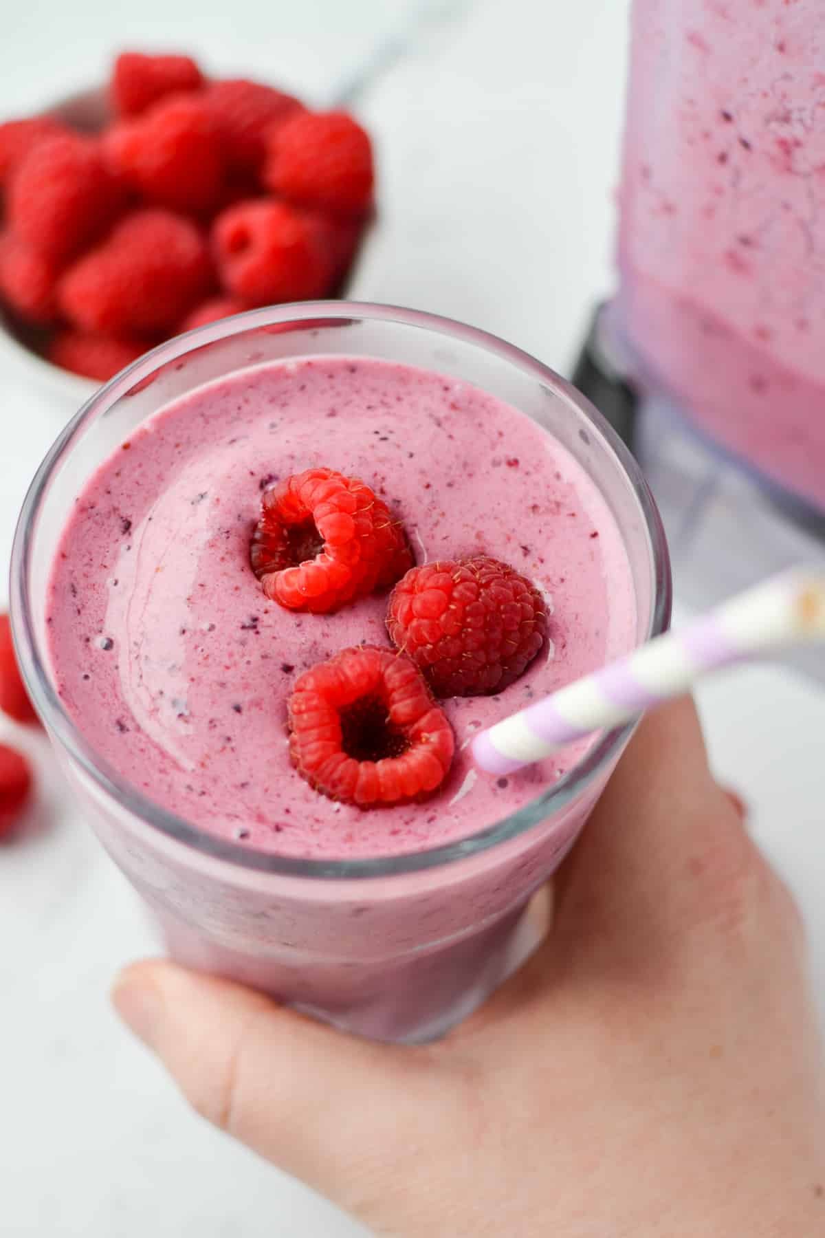 A hand taking a glass of blended fruit topped with raspberries.