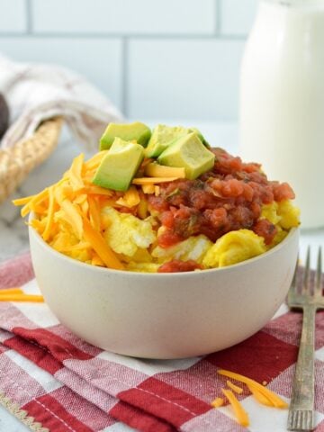 A bowl of scrambled eggs with cheese, salsa, and avocado as toppings.