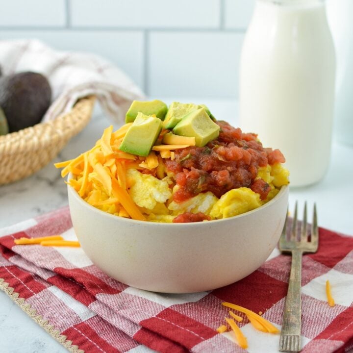 A bowl of scrambled eggs with cheese, salsa, and avocado as toppings.