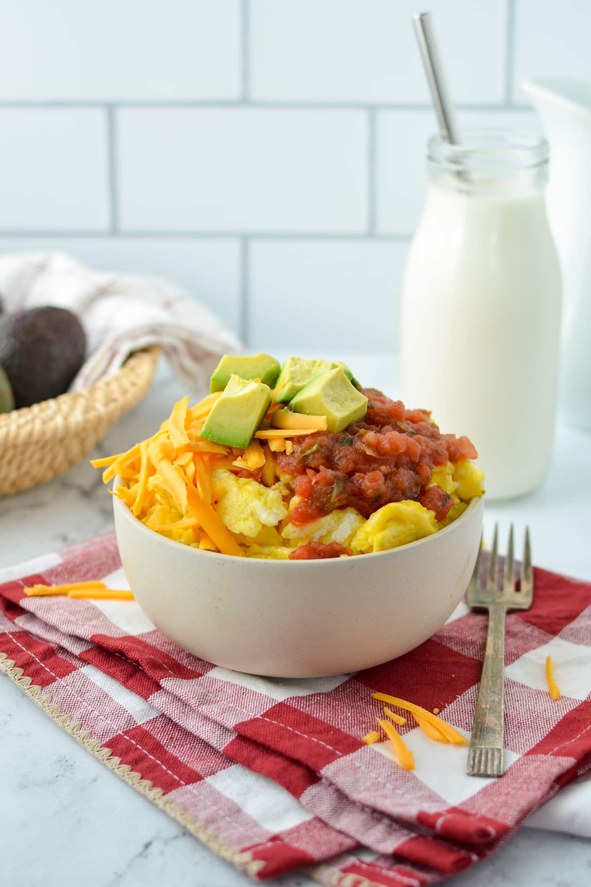 A bowl with scrambled eggs, topped with salsa, cheese, and avocado.