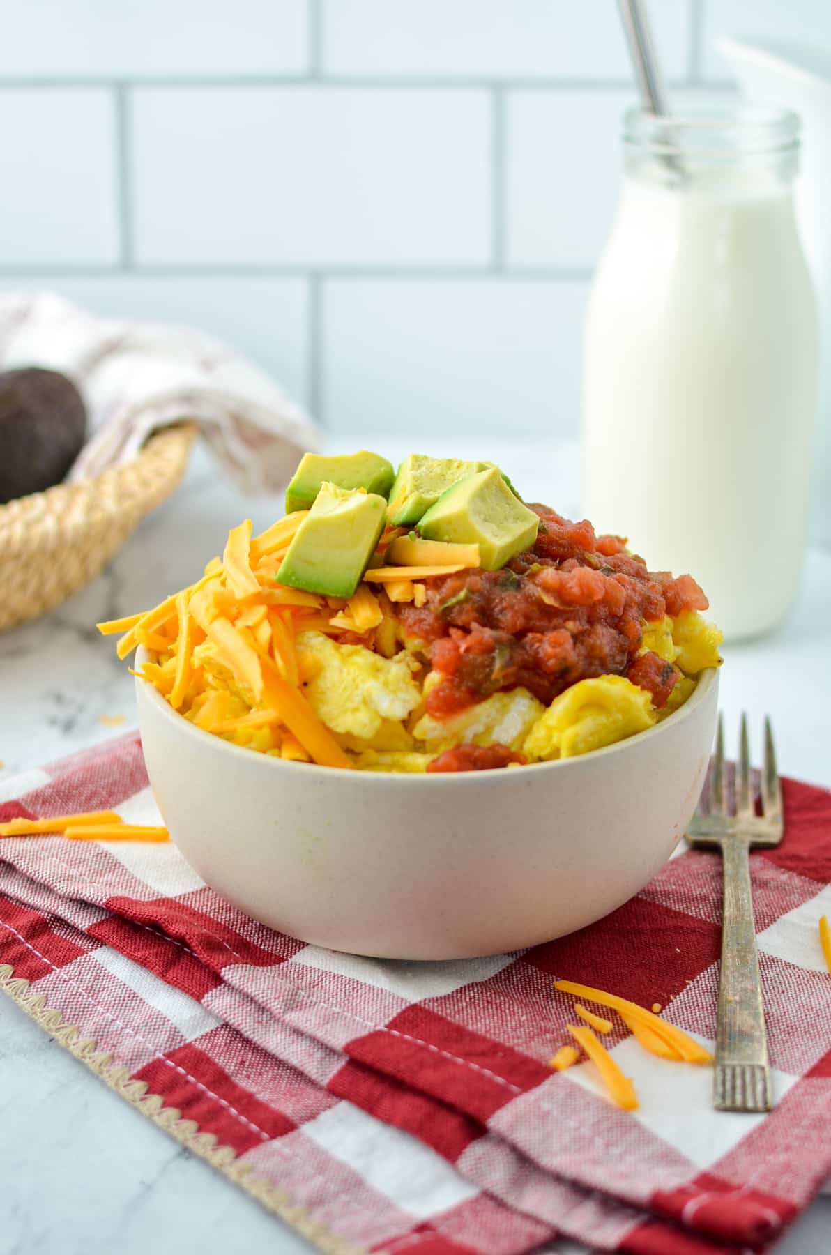 A bowl with eggs, cheese, salsa, and avocado.