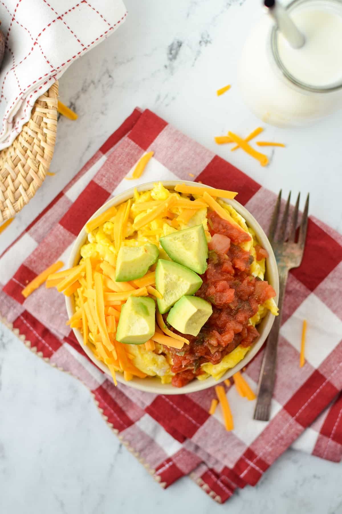 An overhead view of a bowl with scrambled eggs and toppings.