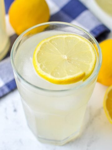 A glass of lemonade finished with a garnish of a slice of lemon.