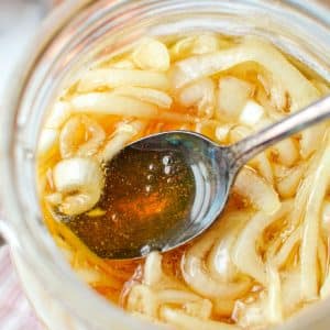 A jar with onions and honey, with a spoon taking a portion.