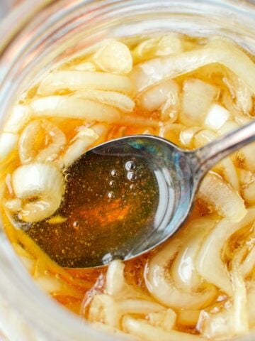 A jar with onions and honey, with a spoon taking a portion.