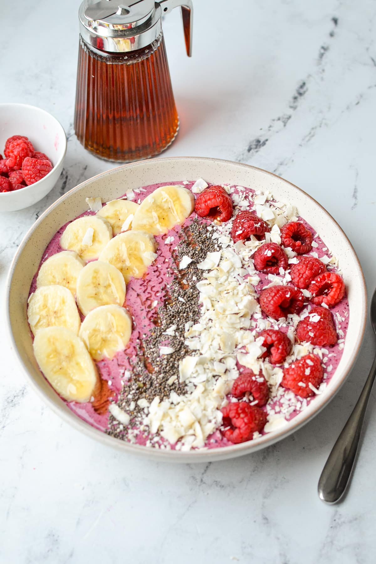 A smoothie bowl topped with banana, chia, coconut, and raspberries.
