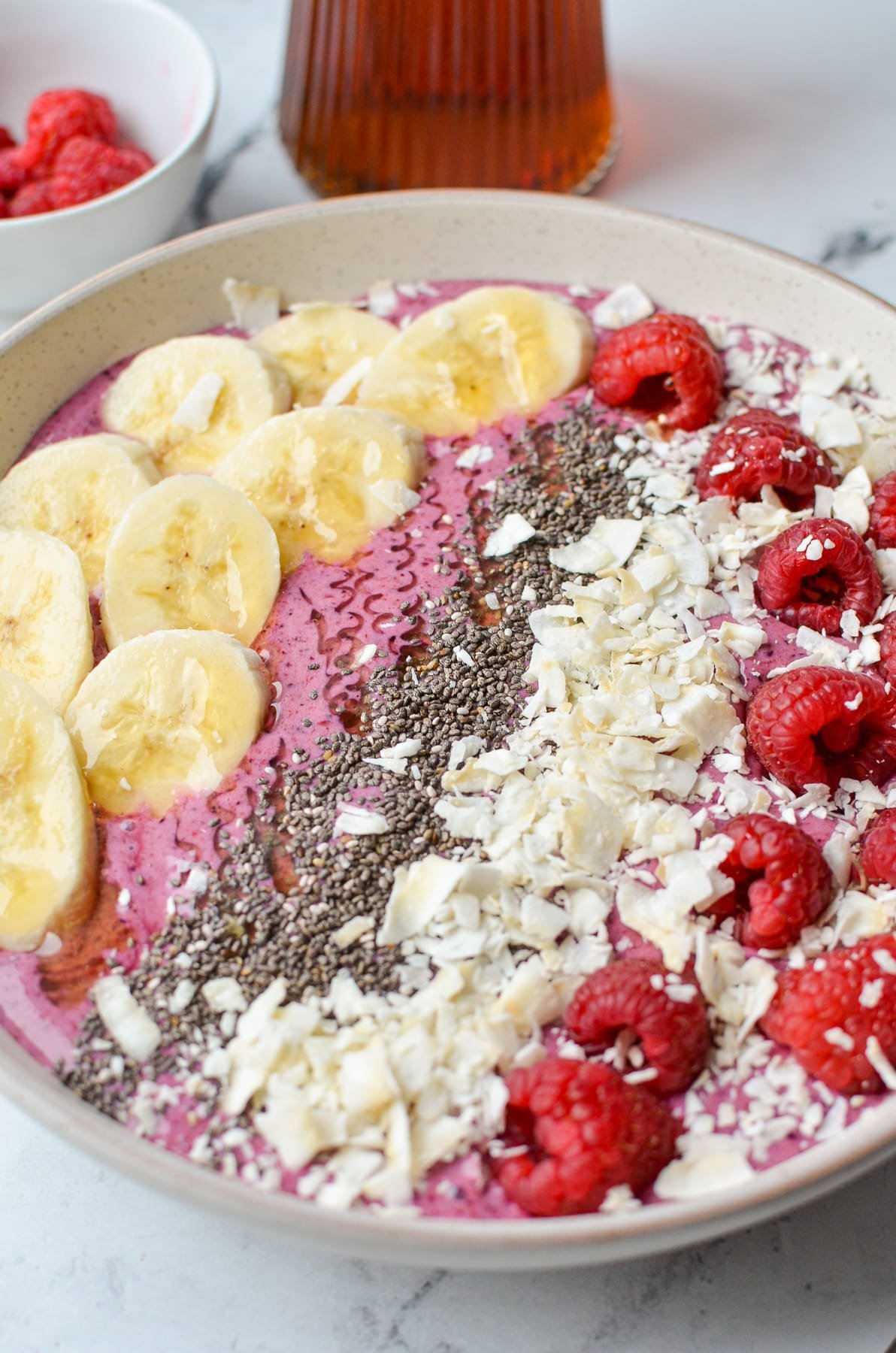 A close up of a smoothie bowl with banana, chia, coconut, and raspberries.