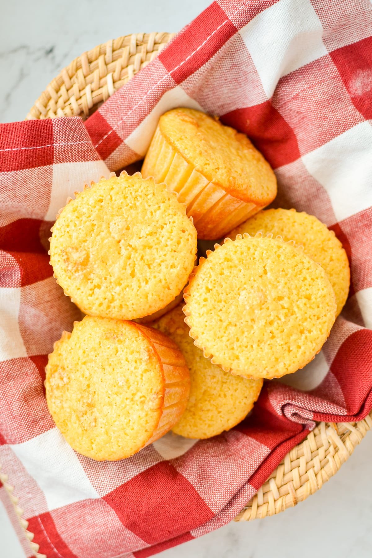 Corn muffins laying inside of a red check napkin-lined bowl.