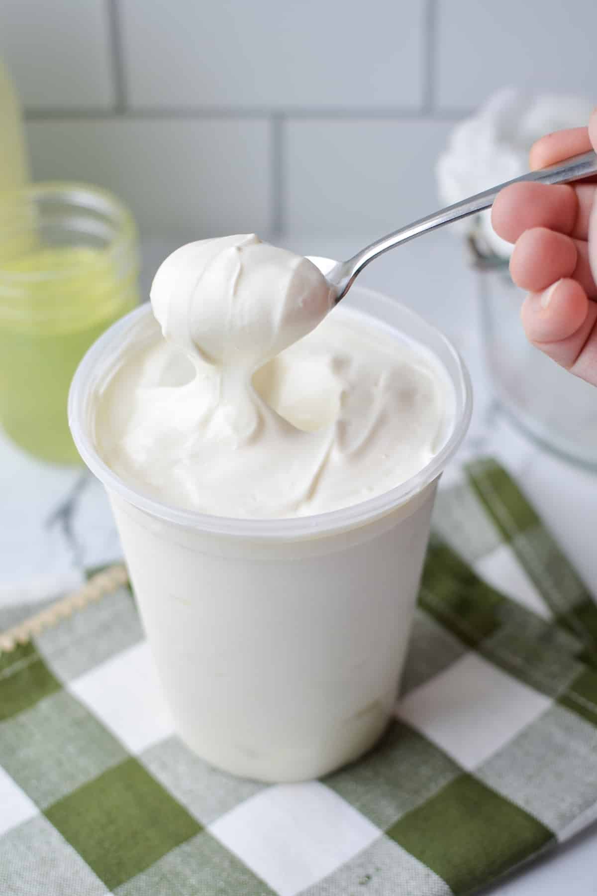 A container with thick Greek yogurt, with a spoon taking a portion.