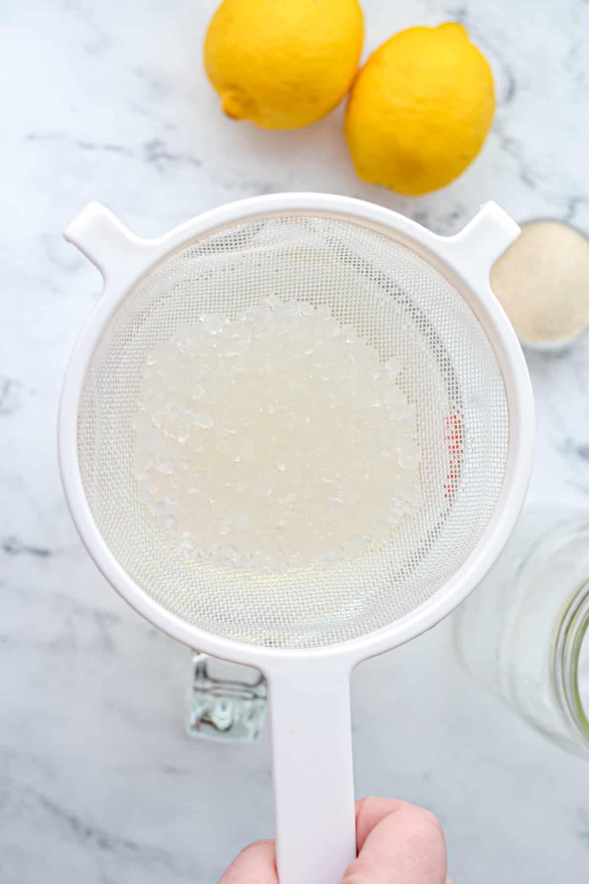 Using a mesh strainer to strain water kefir grains.