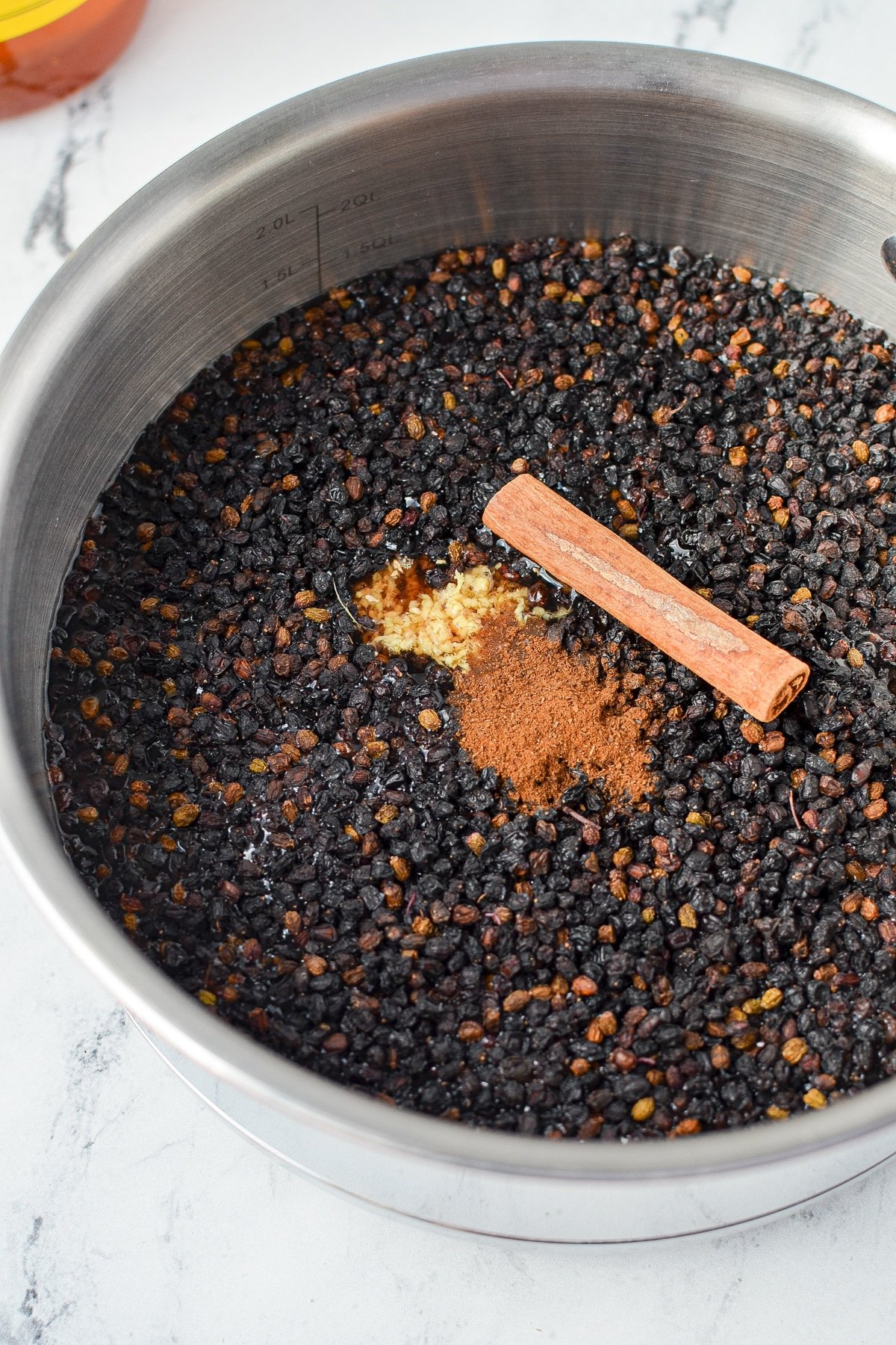 A saucepan with elderberries, cinnamon, ginger, and cloves.