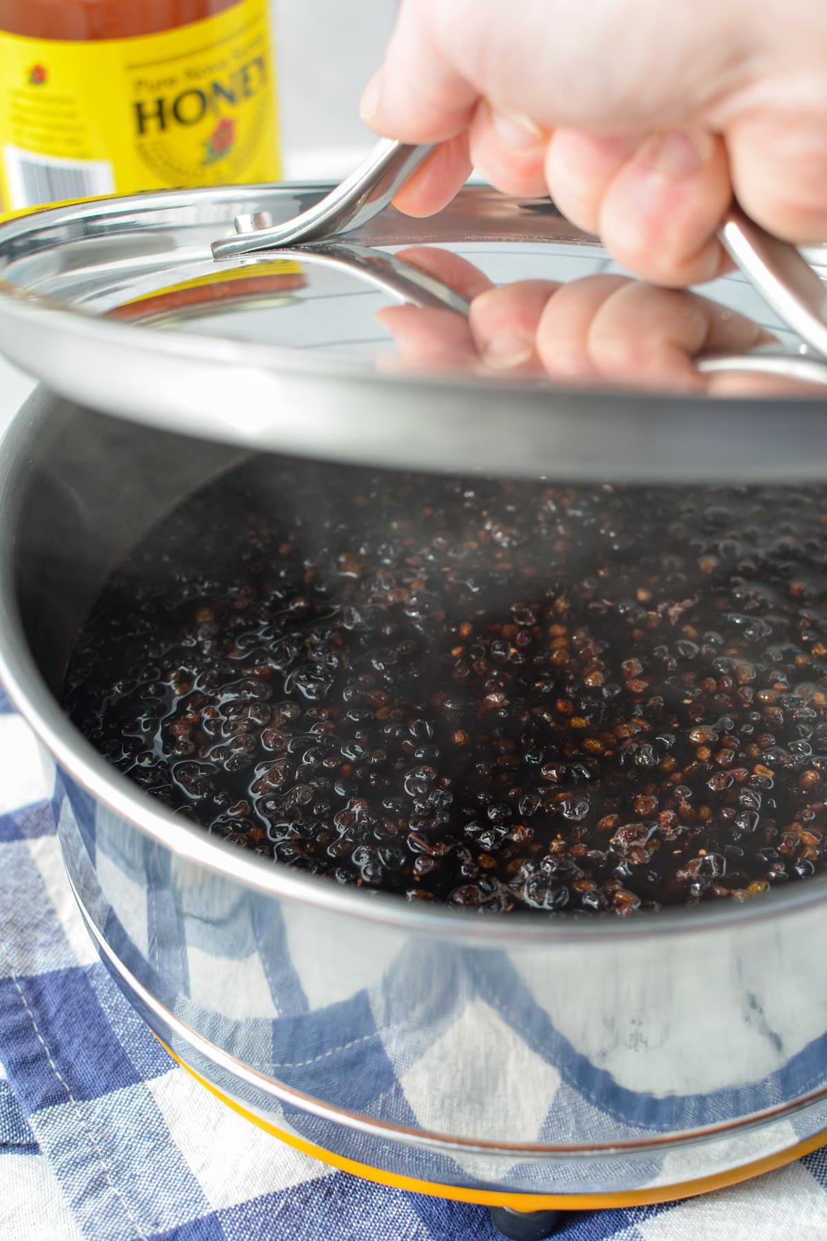 Placing a pot lid on a saucepan of simmering fruit and water.