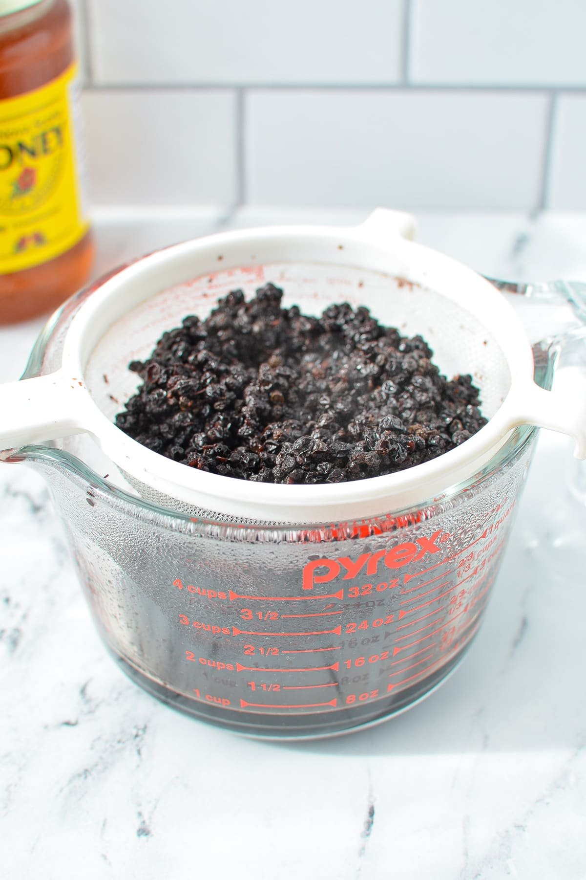 A measuring cup with a strainer set over it, collecting the juices from draining elderberries.
