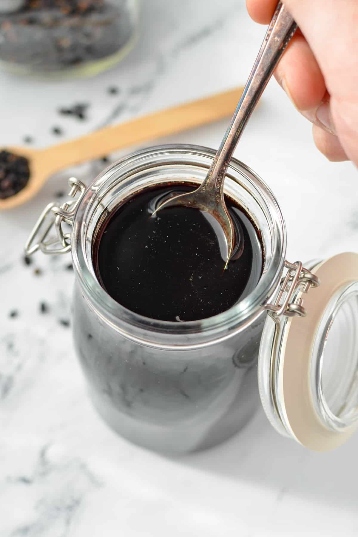 Using a spoon to take elderberry syrup from a jar.