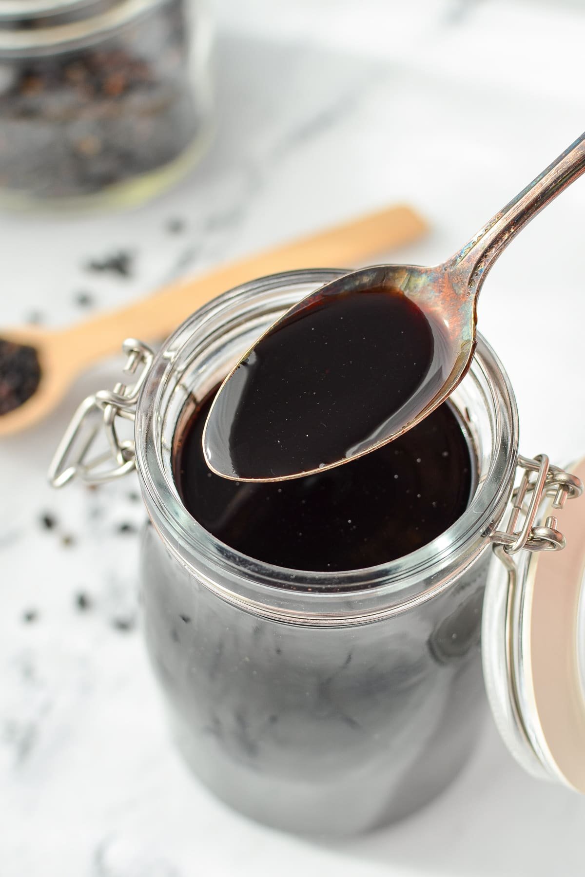 A spoon with elderberry syrup, with dried elderberries in the background.