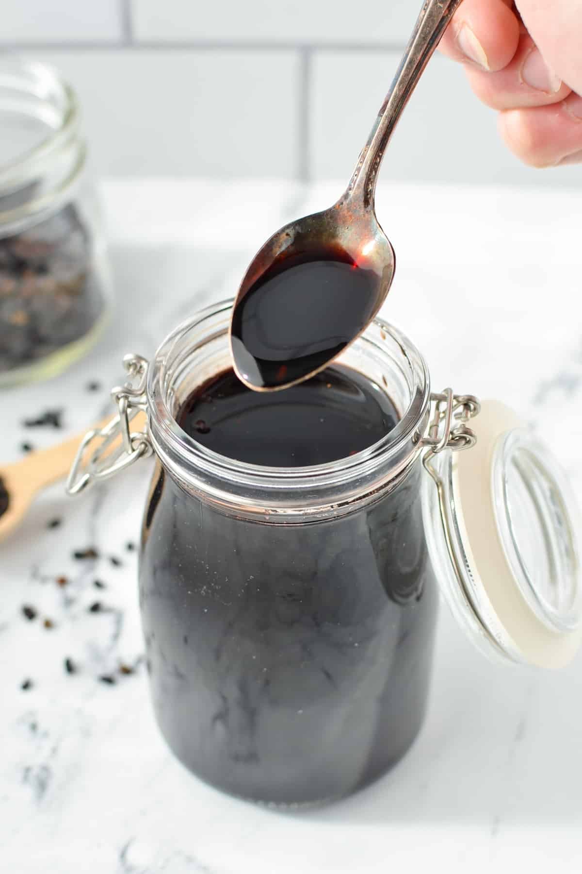 Taking a spoonful of elderberry syrup from a jar.