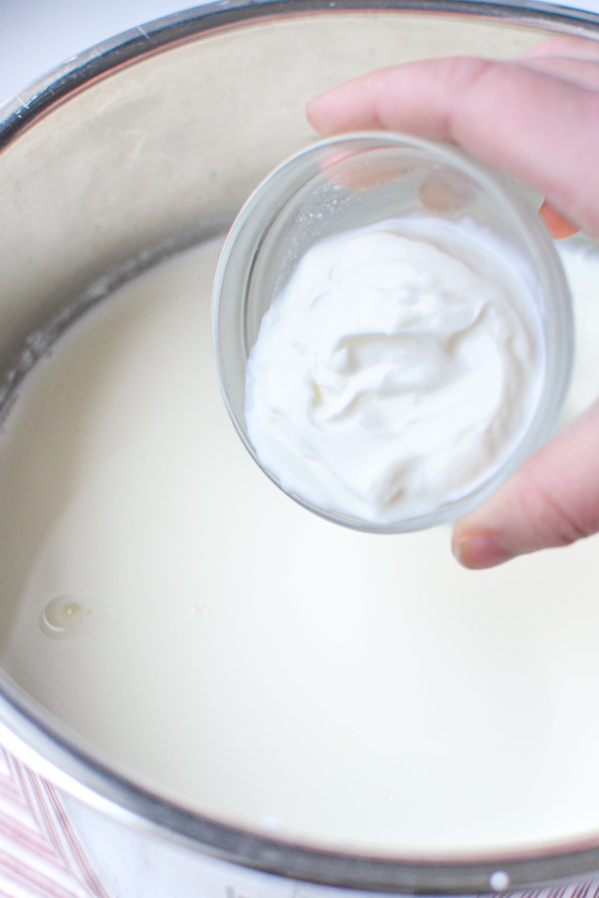 Adding yogurt to a large pot of milk.