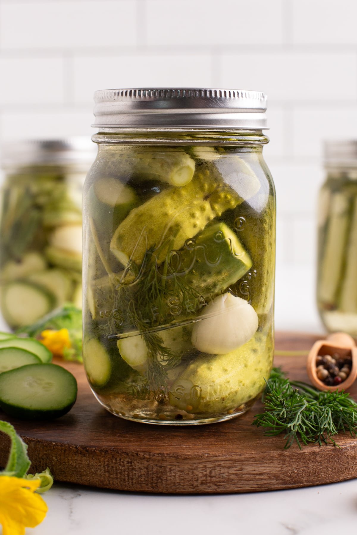 A jar of homemade pickles on a wood cutting board.