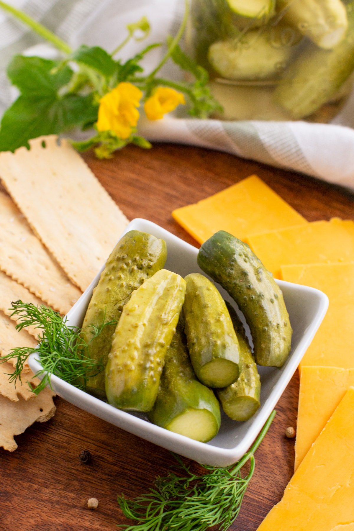 A small dish of pickles with cheese and crackers around the table in behind it.