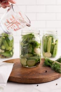 Pouring pickling brine on top of jars of cucumbers.