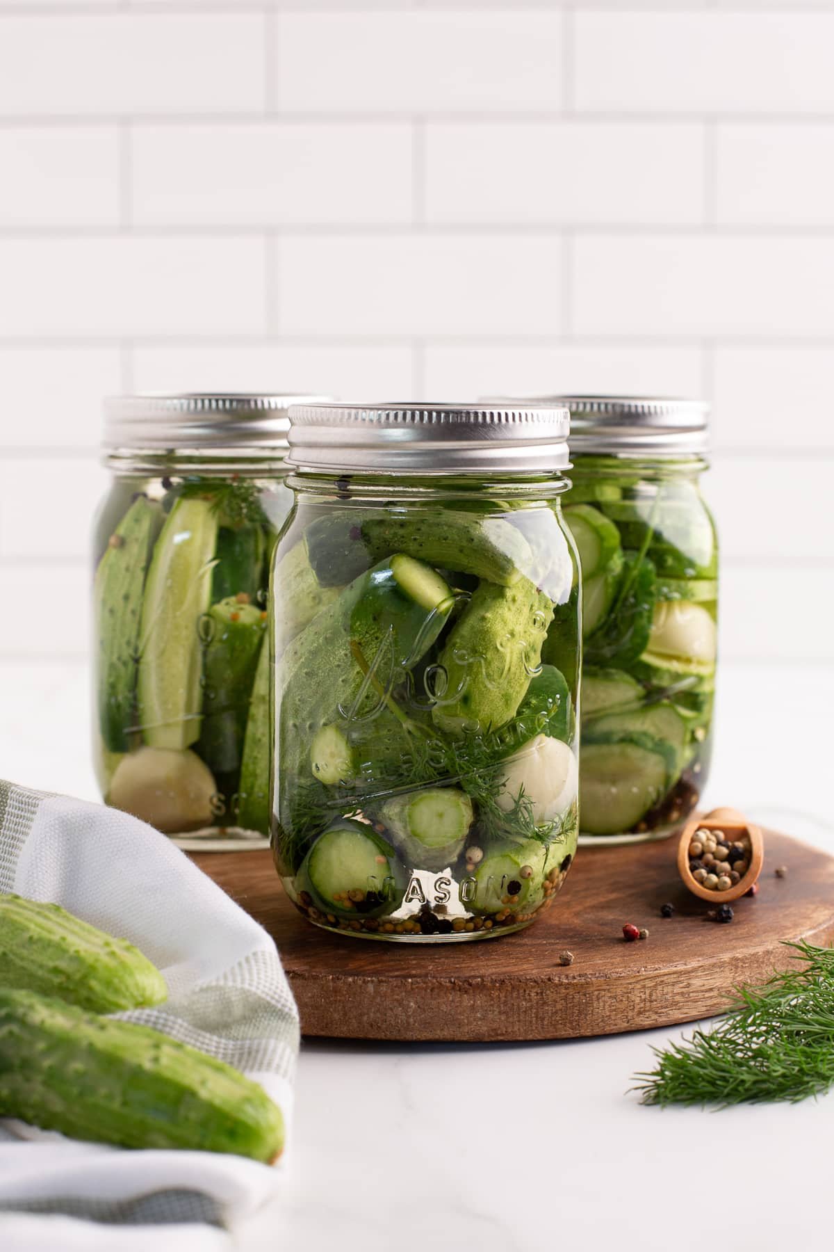 3 jars of dill pickles on a wood cutting board.