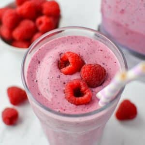 A glass filled with a berry smoothie and topped with fresh raspberries.